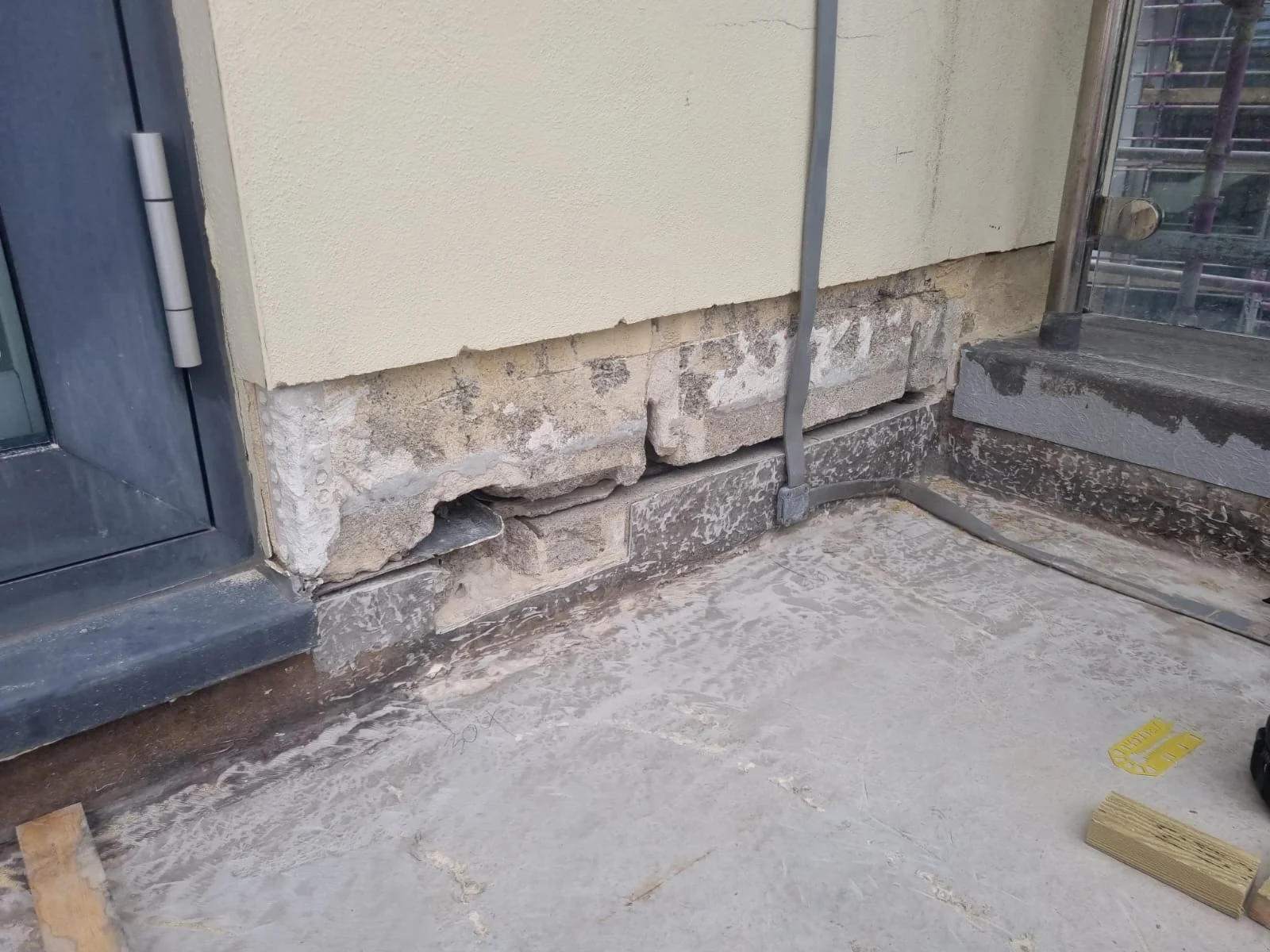 Damaged brickwork and peeling plaster near door corner.