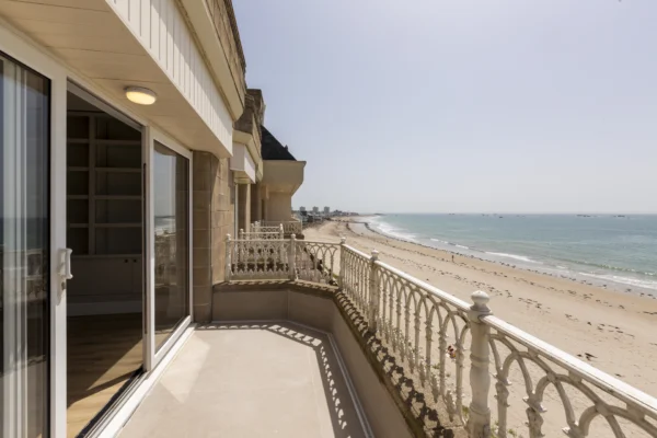 Beachfront balcony view overlooking ocean and sandy shore.